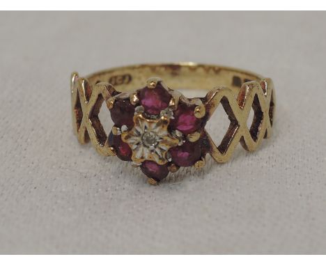 A lady's dress ring having a ruby and diamond chip daisy cluster to open chequered shoulders on a 9ct gold loop, size O