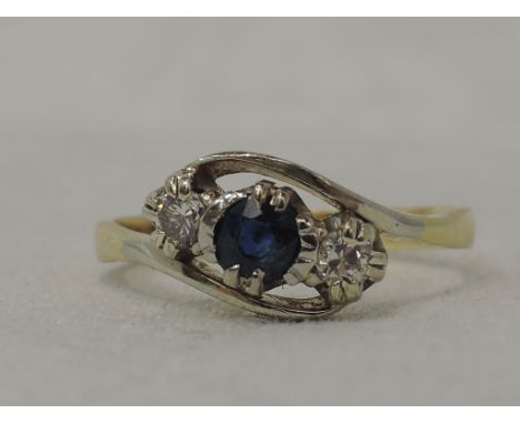 A lady's dress ring having a central sapphire flanked by two diamonds in a claw set mount to cross over shoulders on a yellow