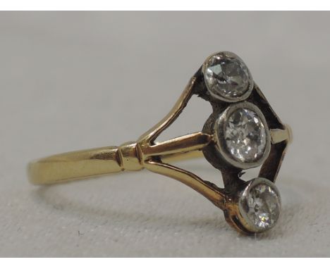 A lady's dress ring having a vertical set trilogy of diamonds in collared mounts to open shoulders on a yellow metal loop sta