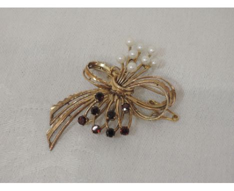 A 9ct gold brooch modelled as a stylised bow having seed pearl and garnet decoration