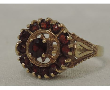 A lady's dress ring having an open garnet cluster in a raised claw set mount to open shoulders on a 9ct gold loop,  size N