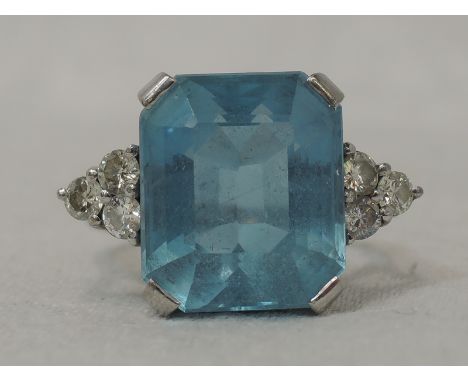 A lady's dress ring having a large emerald cut aqua marine, approx 5ct in a four claw mount flanked by a trio of diamonds to 