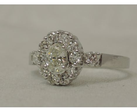 A lady's dress ring having an oval diamond cluster to diamond set shoulders on a white metal loop stamped 750, size PNO VISIB