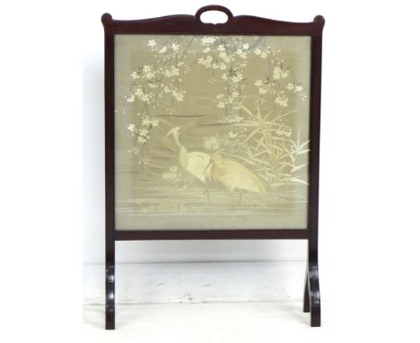 An Edwardian mahogany fire screen, inset with an embroidered panel under glass, depicting two herons standing in water below 