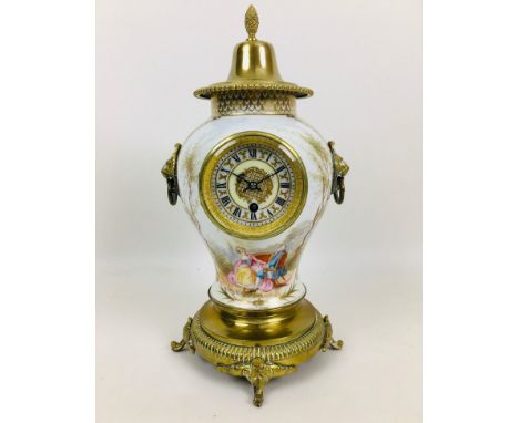 A late 19th century porcelain vase clock, with a brass cover and mounted on circular metal base with four feet, lion's mask h