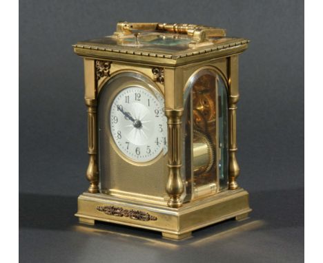 FRENCH BRASS FOUR PANE CARRIAGE CLOCK, the silvered dial with engine turned centre in an arched gilt frame with scrolling spa