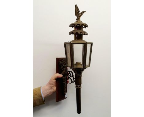 An early 20th century brass oil carriage lamp, with an eagle finial, 59 cm high, mounted on a wooden panel and an early 20th 