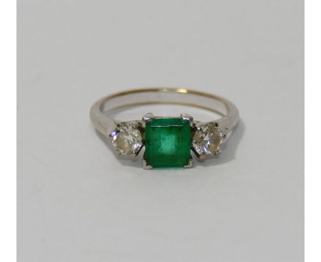 An emerald and diamond three stone ring, the baguette cut emerald in four claw setting, approximately 0.96 carats, set within