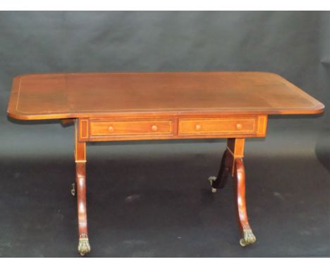 A Regency style mahogany sofa table with crossbanding and inlaid lines on twin supports with sabre legs and brass capped cast