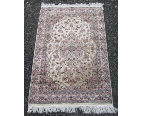 An Indian rug, the ivory field with a light brown medallion, with scrolling vines, leaves and palmettes, within a similar bor