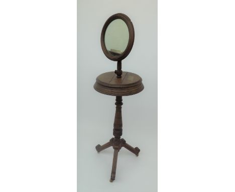 A late Victorian mahogany shaving stand, with angular tripod base, circular mirror and a shelf with twin lidded compartments.