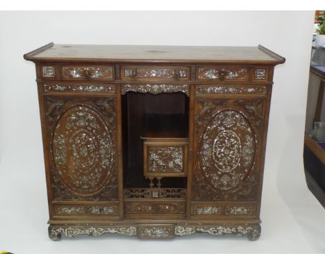 A Chinese hardwood cabinet, circa 1900, profusely inlaid with mother of pearl, with three frieze drawers decorated with flora