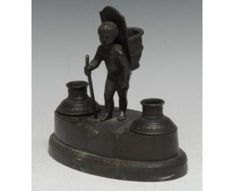 A French Empire dark patinated bronze desk stand, cast with a young grape picker, his hod for spills, flanked by inkwell and 