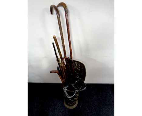 A brass embossed stick stand containing a quantity of walking sticks and crooks, together with a shooting stick 