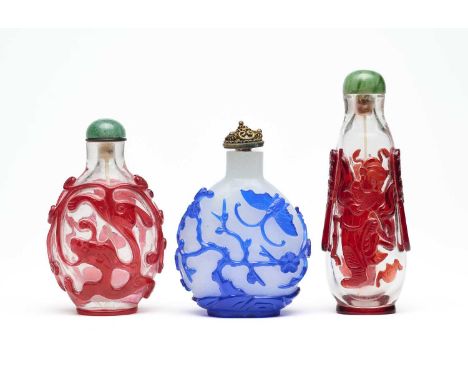 THREE CHINESE CARVED OVERLAY GLASS SNUFF BOTTLES  comprising: a ruby-red overlay clear glass pear-shaped bottle, carved to ea