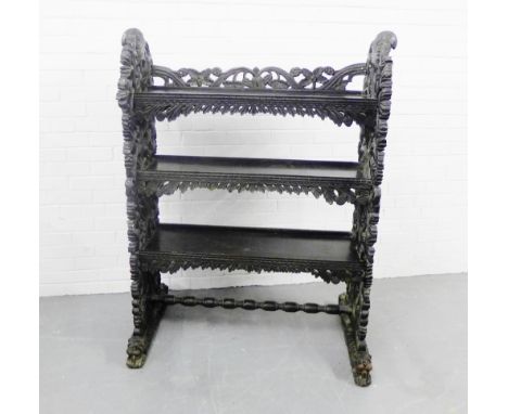 An Eastern three tier book shelf on foliate and fruit carved end supports with a turned stretcher terminating on further carv