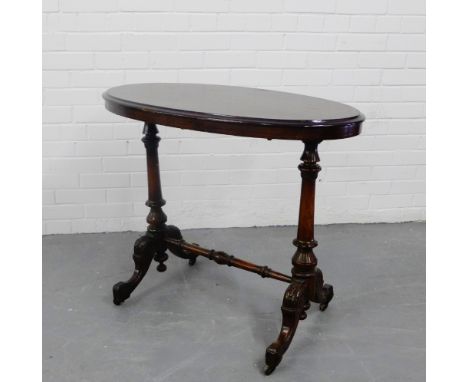 A mahogany side table, the oval top on turned twin column supports and undertier, terminating in ceramic castors, 74 x 90cm