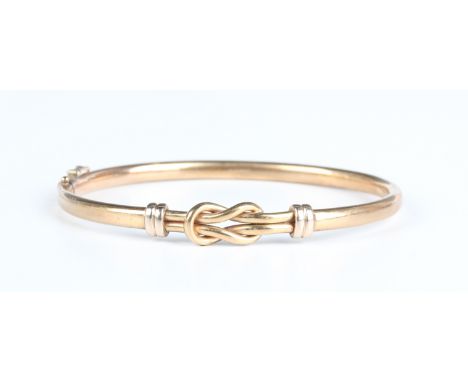 A gold oval hinged bangle, the front with a knot motif, on a snap clasp, detailed '375', weight 9.3g, inside width 6cm.Buyer’