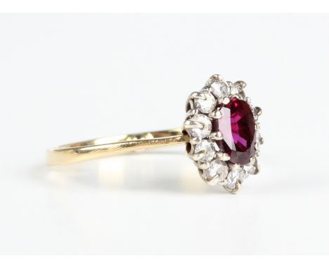 An 18ct gold, ruby and diamond oval cluster ring, claw set with the oval cut ruby within a surround of circular cut diamonds,