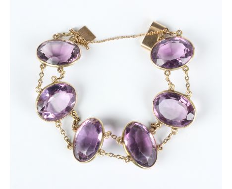 An Edwardian gold and amethyst bracelet, circa 1910, spectacle set with a row of six large graduated oval cut amethysts, on a