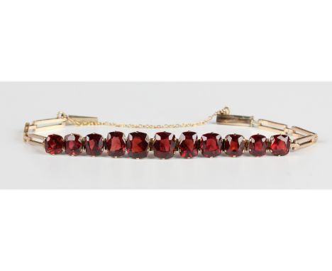 A gold and garnet bracelet, 1920s/30s, claw set with a row of eleven cushion cut garnets graduating in size to the centre sto