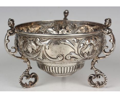 An Edwardian silver bowl of circular form, embossed with flowers and foliate scrolls, raised on three caryatid scroll legs, L