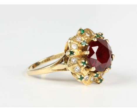 An 18ct gold ring, claw set with a circular cut garnet within a shaped surround, mounted with circular cut diamonds and emera