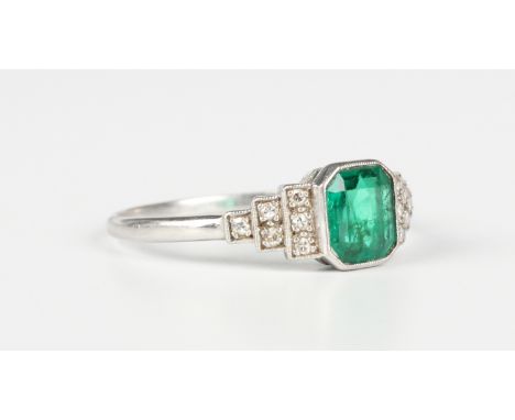 A platinum, emerald and diamond ring, mounted with a cut cornered rectangular cut emerald between diamond set stepped shoulde