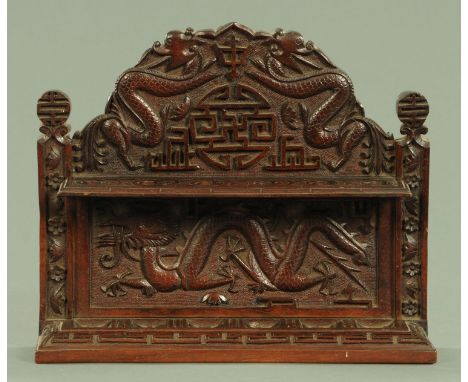 A carved hardwood pipe rack, early 20th century, carved with dragons flanking a Shou symbol, flanked by pilasters with floral