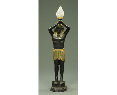 A lamp standard, in the form of a male Egyptian figure holding aloft a flaming torch, raised on an octagonal base, painted me