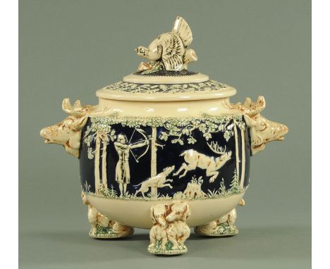 A late 19th century soup tureen, relief moulded with hunting scenes in woodland and with stags head handles and Dachshund fee