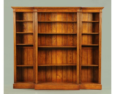 An oak breakfront open bookcase, with moulded dentil cornice above a series of adjustable shelves and raised on a plinth.  Wi