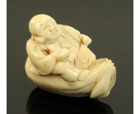 A Japanese ivory Netsuke, circa 1880, carved as Hotei seated upon his sack of treasures, signed, 3.5 cm long, CONDITION REPOR