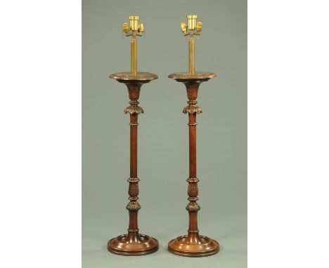A pair of carved mahogany lamp standards, foliate and bellflower carved and with circular bases.  Height including light fitt