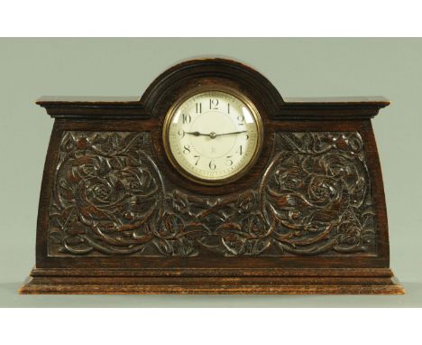 An Arts and Crafts carved oak mantle clock, circa 1900, the enamel dial with Arabic numerals and French movement within a car