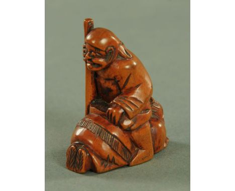 A Japanese carved softwood Netsuke, circa 1900, depicting a man with a staff seated astride a further grimacing male figure, 
