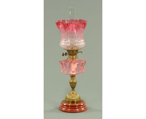A Victorian oil lamp, with cranberry glass shade and reservoir, brass column and raised on a ceramic base.  Height including 