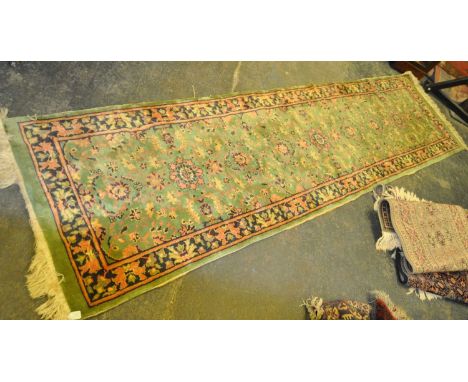 A 20th century Persian manner runner carpet rug. The rug having a green ground with pink detailing, having floral motifs popu