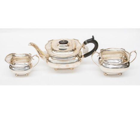 A George V silver three piece tea set, plain bodies with wavy rim on four stud feet, the teapot with ebony C-scroll handle an