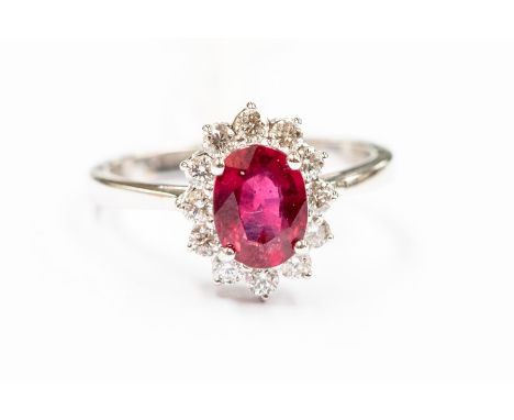 A ruby and diamond 18ct white gold ring, comprising a claw set oval ruby set to the centre within a border of brilliant cut d