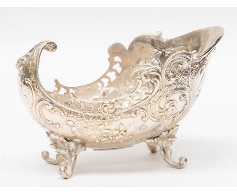 A late Victorian silver sugar bowl, stylised slipper shaped chased with scrolling foliage, openwork border and raised on four