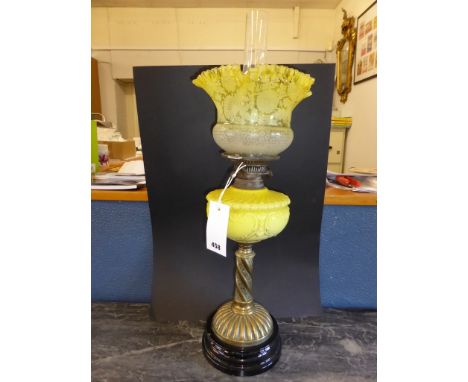 An antique oil lamp with brass column, yellow glass reservoir & shade.