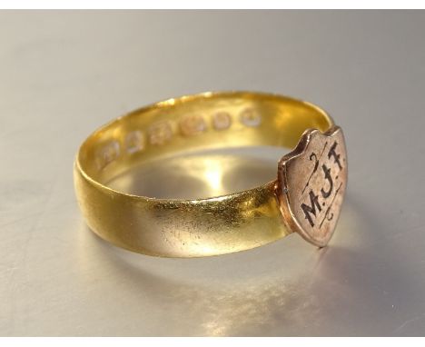 A gold wedding band with small initialled shield attached, (marks obliterated), size M, 3g. 