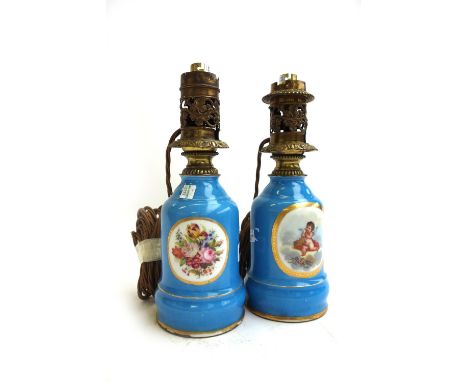 A pair of porcelain oil lamp bases (converted), each decorated with Cupid figures and still life flowers against a gilt and b