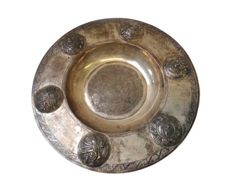 A Mexican alms dish, of circular form, decorated with a central mythological profile, the wide rim with six raised circular b