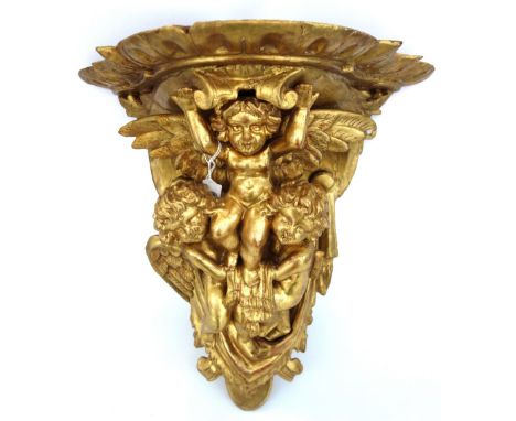 A giltwood carved figural wall bracket, 19th century, the shaped top supported by three putti against a swagged backplate (a.