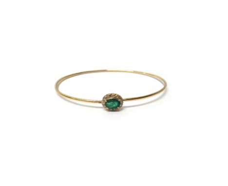 A gold, emerald and diamond set oval cluster bangle, of sprung form, claw set with the oval cut ruby at the centre, in a surr