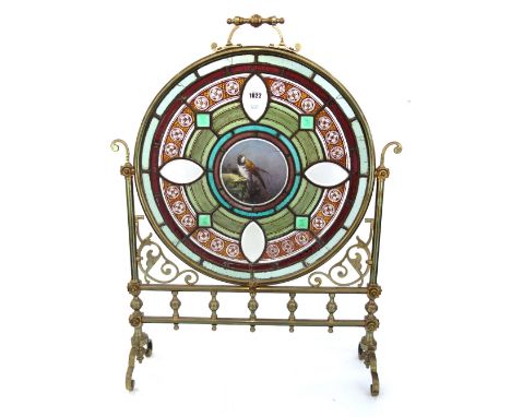 A Victorian brass and glass mounted fire screen of Gothic style, the circular frame inset with a coloured glass panel centred
