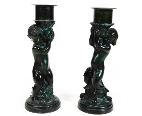 A pair of patenated bronze finish candlestick figures, each with urn dish holders, raised on cherubic stems with naturalistic