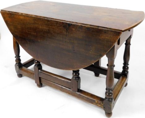 A Jacobean style oak gate leg drop leaf table, with plank top, on turned supports terminating in compressed orb feet joined b